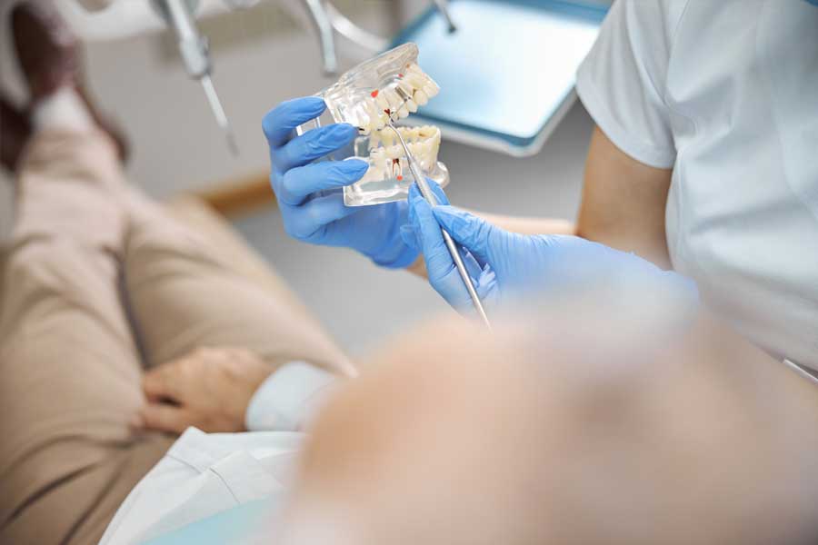 Dental professional explaining oral surgery treatment using a teeth model during patient consultation.